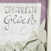 Detailaufnahme des Geschenk-Rahmens zum Polterabend oder zur Hochzeit. Im weißen Rahmen wird ein Haufen Porzellan-Scherben und der Schriftzug 