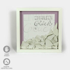 Idee für Geschenk-Rahmen zum Polterabend oder zur Hochzeit. Der weiße Rahmen wurde mit vielen Porzellan-Scherben dekoriert und enthält im Hintergrund den Schriftzug "Ein Haufen Glück"