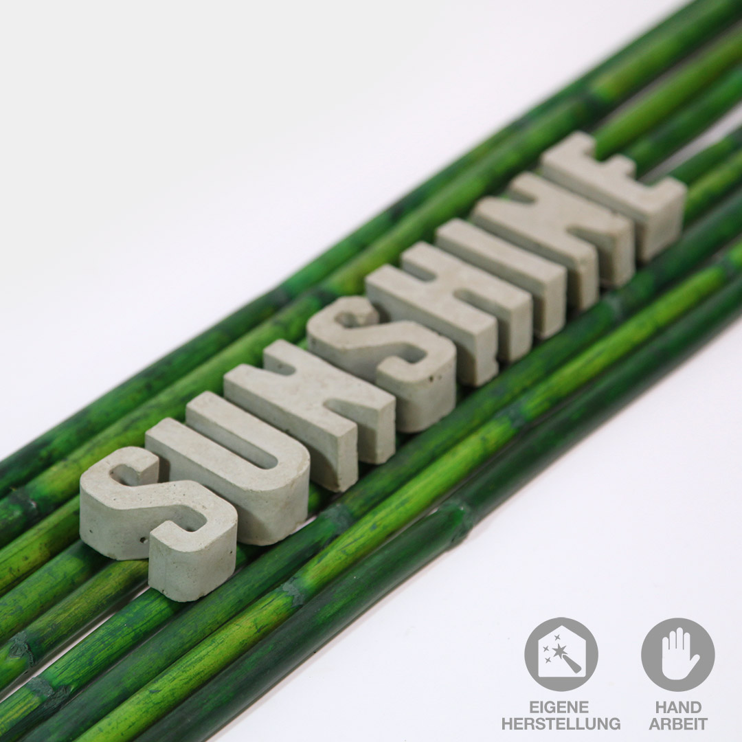 Handgefertigte Buchstaben aus Beton. Hier das Wort "SUNSHINE" liegend auf Bambusstangen.