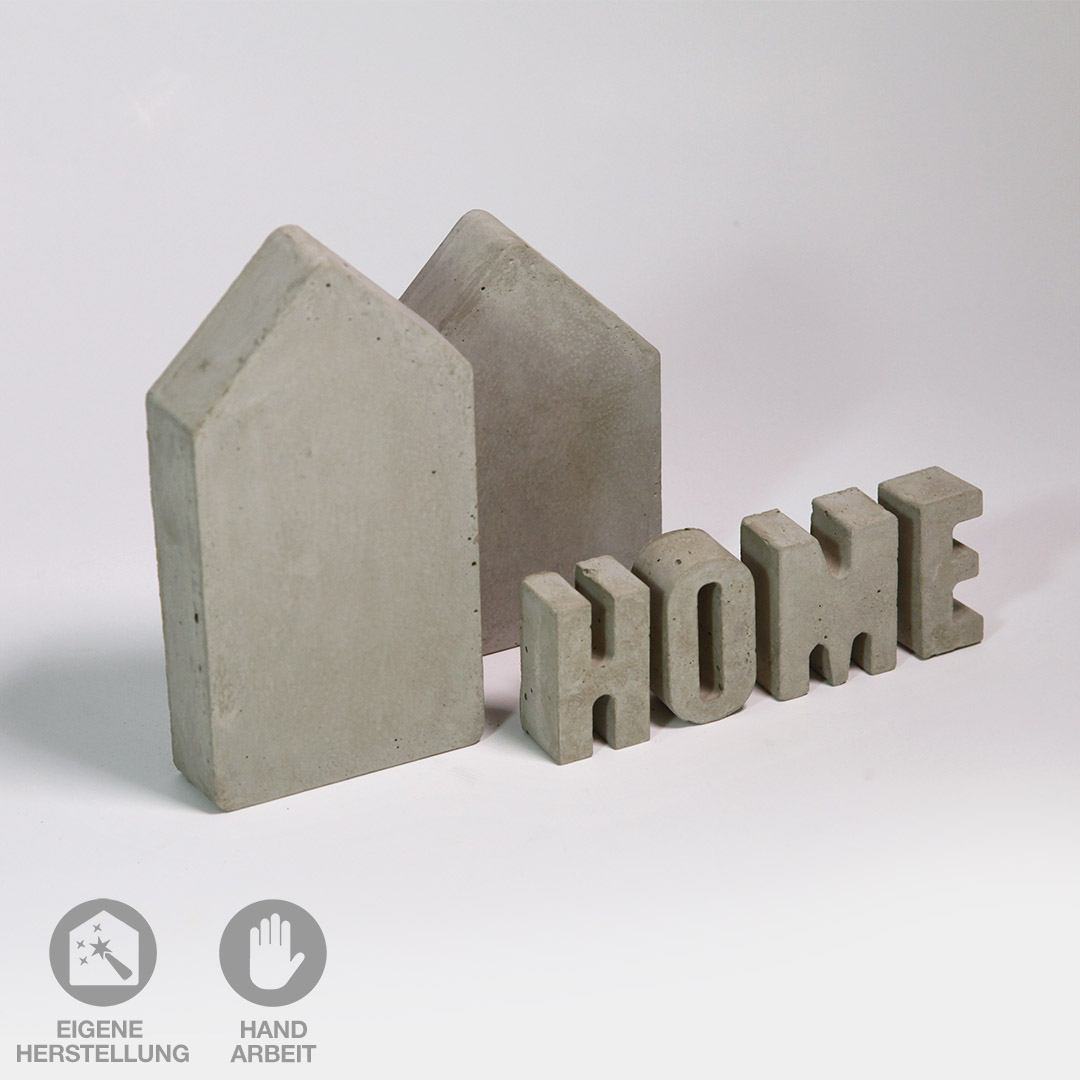 Zwei handgefertigte Beton-Häuser mit dem Beton-Schriftzug "HOME" in Großbuchstaben.