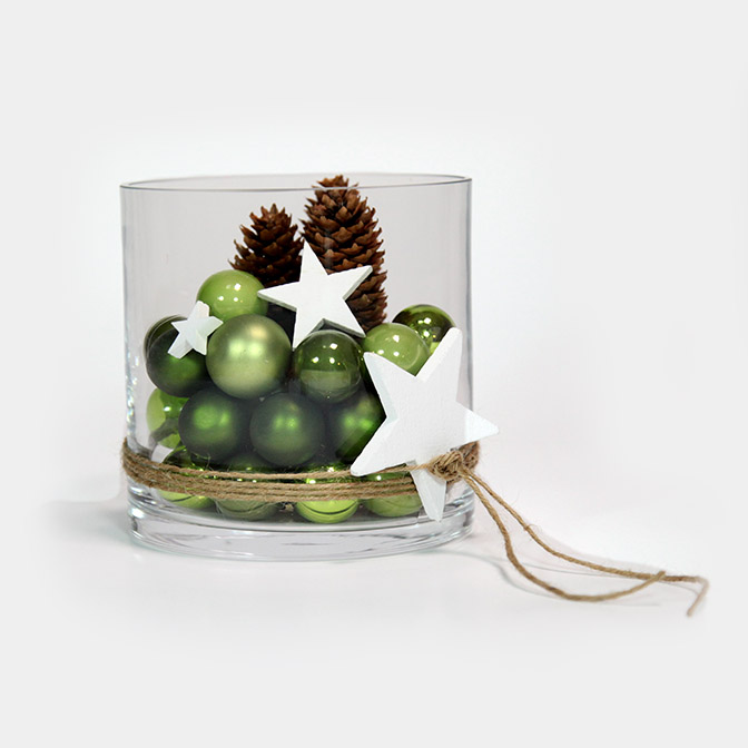 Wunderschöne Glas-Vase dekoriert mit einem Farbmix aus grünen Weihnachtsbaum-Kugeln. Dazu wurden weiße Holz-Sterne und Tannenzapfen dekoriert. Um es abzurunden ist die Vase mit einer Natur-Kordel umwickelt und einem Holz-Stern versehen.
