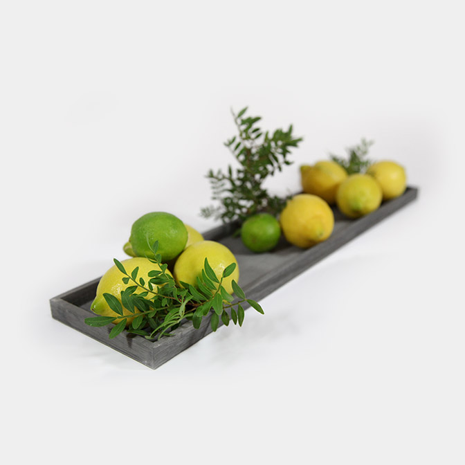Wunderschönes, schlichtes, graues Holz-Tablett. Diese Deko-Beispiel zeigt es mit Zitronen, Limetten und Pistazien-Zweigen.