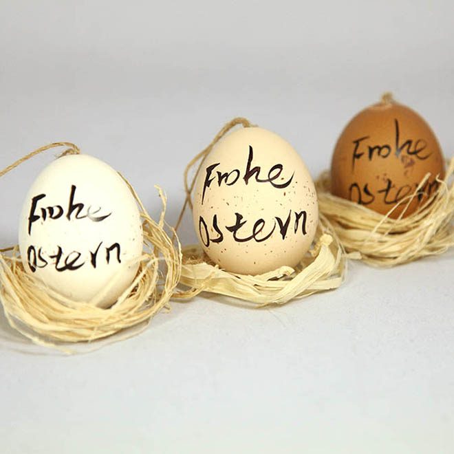 Drei Hühner-Eier bemalt mit "Frohe Ostern" in weiß, beige und braun.