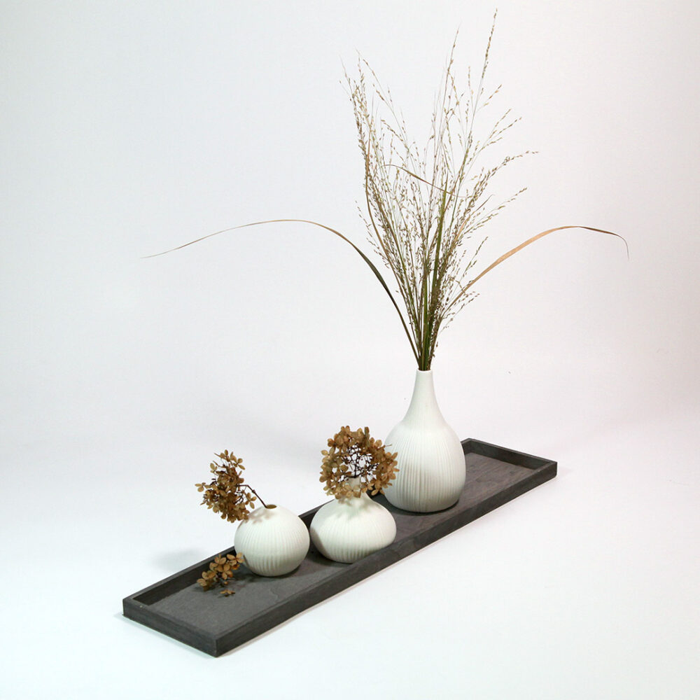Tischdekoration im Scandi-Style. Graues Holz-Tablett mit drei weißen Vasen bestückt mit Trocken-Blumen und-Gräsern.