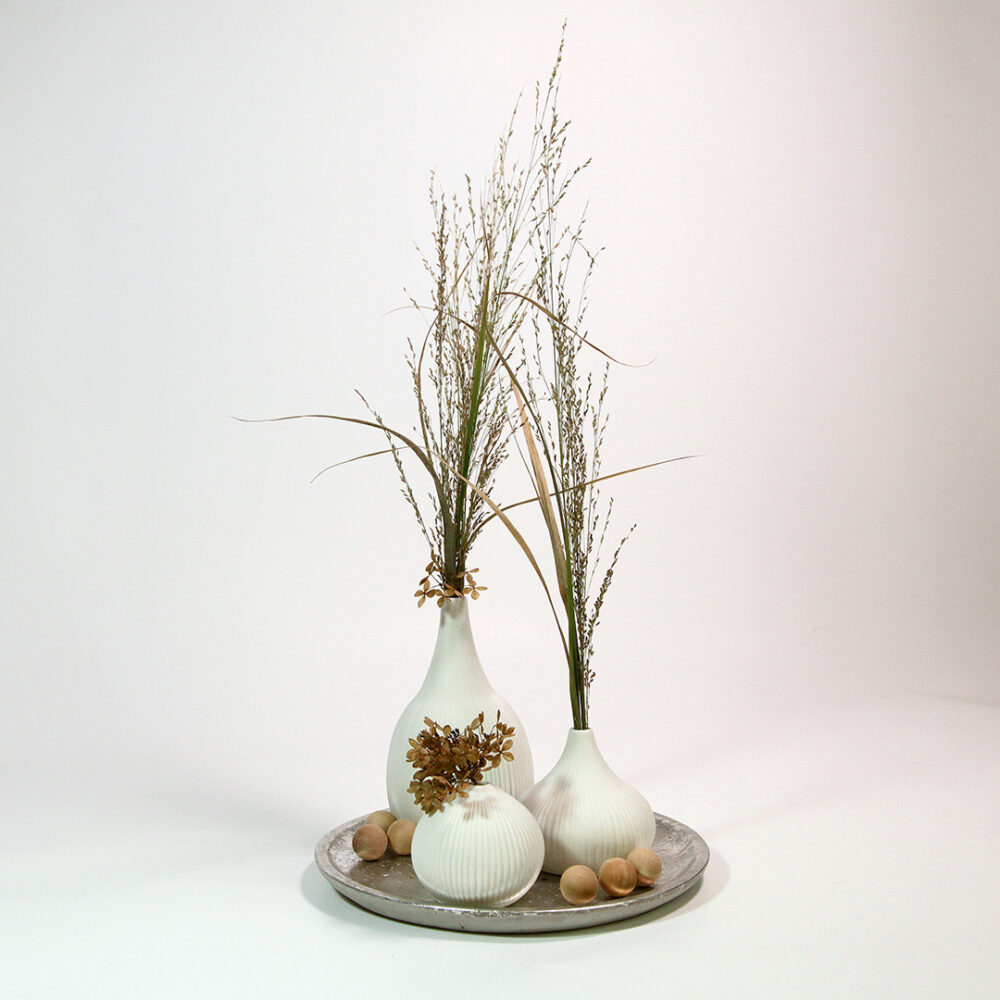 Dekorativer silberner Deko-Teller mit drei weißen Keramik-Vasen. Unsere Scandi-Style-Deko ist geschmückt mit Holz-Kugeln, Trocken-Blumen und Gräsern.
