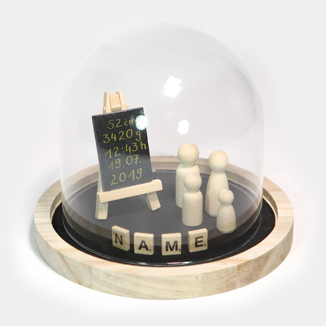 Diese schlichte, dekorative Glas-Haube steht auf einem runden Holz-Tablett. Dieses ist bestückt mit der jeweiligen Anzahl der Familienmitgliedern, symbolisiert durch Holz-Figuren, einer Schiefern-Tafel und denen von Ihnen gewünschten Namens-Blättchen.