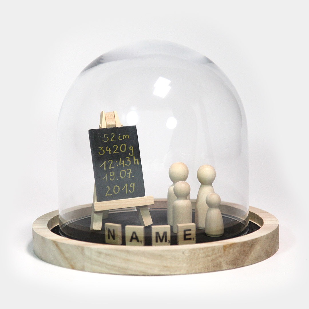 Persönliche Geschenkidee zur Geburt. Diese schlichte, dekorative Glas-Haube steht auf einem runden Holz-Tablett. Dieses ist bestückt mit der jeweiligen Anzahl der Familienmitgliedern, symbolisiert durch Holz-Figuren, einer Schiefern-Tafel und denen von Ihnen gewünschten Namens-Blättchen.