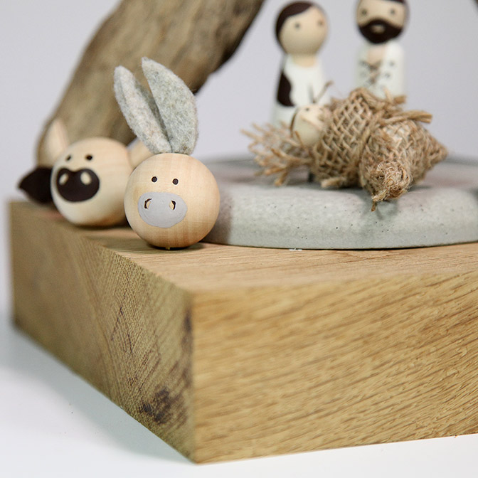 Ausschnitt von einer Hand bemalten Weihnachts-Krippe mit Maria,l Josef, dem Jesuskind und Ochse und Esel. Präsentiert auf einer Betonplatte.