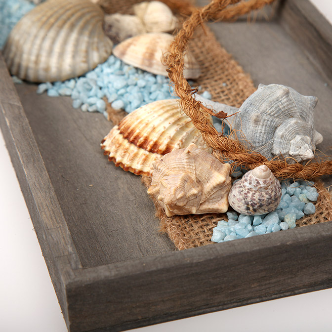 Deko-Tablett mit Leuchtturm "Eine Prise Meer" 6 Ausschnitt aus unserem rechteckigen grauen Holztablett dekoriert mit einem Leuchtturm, Muscheln, einem Seil und Deko-Steinen, Alles in weiß, beige und hellblau gehalten.