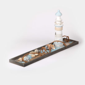 Rechteckiges graues Holztablett dekoriert mit einem Leuchtturm, Muscheln, einem Seil und Deko-Steinen, Alles in weiß, beige und hellblau gehalten.