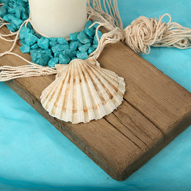 Nahaufnahme von unserem dekorativem Holz-Brett mit Muscheln, türkisfarbenen Deko-Steinen , Netz und wollweißen Kerzen.