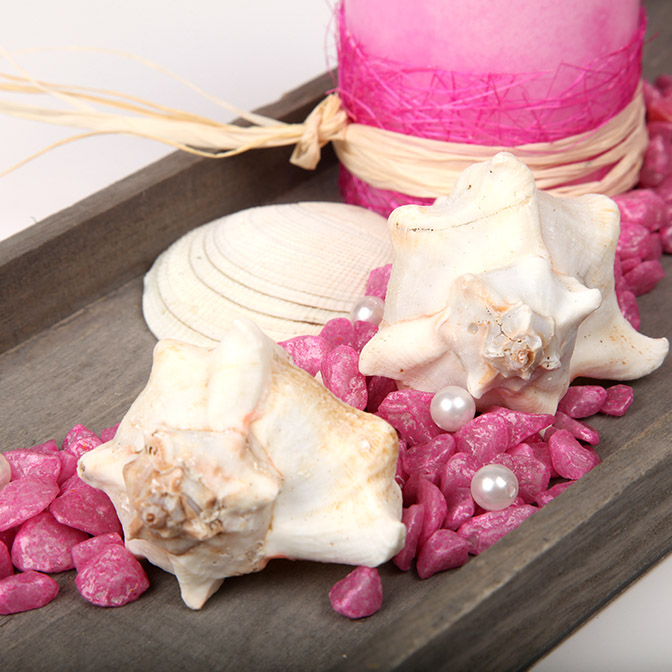 Ein Ausschnitt unseres grauen, rechteckigen Dekotabletts mit Perlen, pinken Kerzen und Deko-Steinen und Muscheln.