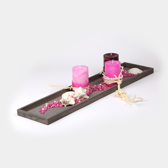 Graues, rechteckiges Dekotablett mit Perlen, pinken Kerzen und Deko-Steinen und Muscheln.