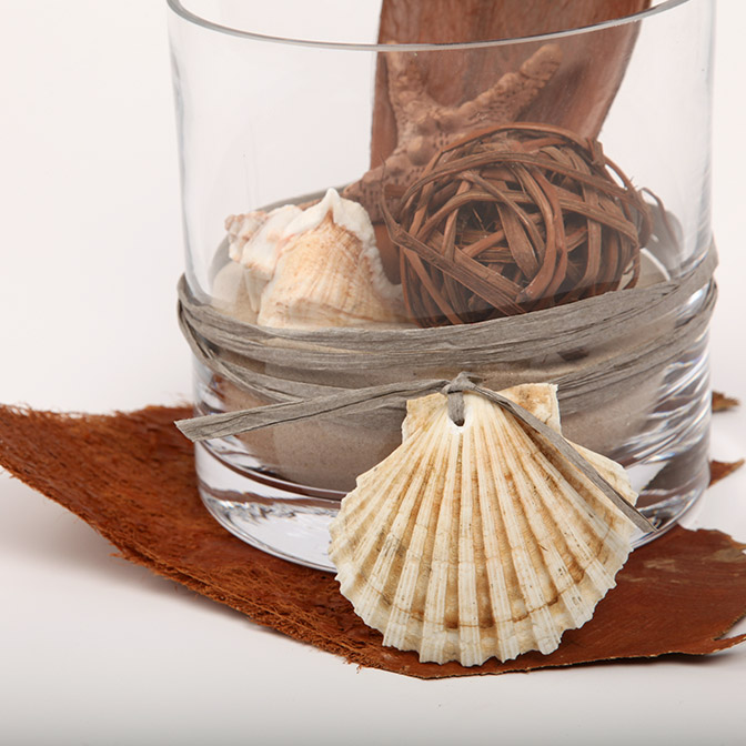 Unser Deko-Vase "Afrika-Safari" besteht aus einem Glas-Zylinder befüllt mit feinstem Quarzsand, welcher sich mit einem Cocos-Schale-Palmenblatt, einem getöpferten Seestern, Muscheln und einer gebundenen Deko-Kugel aus Ästen schmückt. Hier ist nur ein Ausschnitt zu sehen.